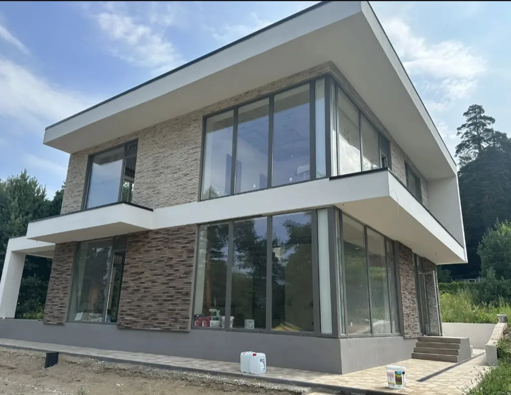 Дом облицованный декоративным кирпичом "Реген Брик" коричневый 690-40, 690-45, "Реген Брик" молочный 694-10, 694-15 (White Hills). Крепится к стене на клей White Hills "Экстра". Для швов использована затирка серая, белая (White Hills). Раскладка брусчатки Steingot Новый город "Травертин", бордюр садовый 1000*200*80 "Травертин".